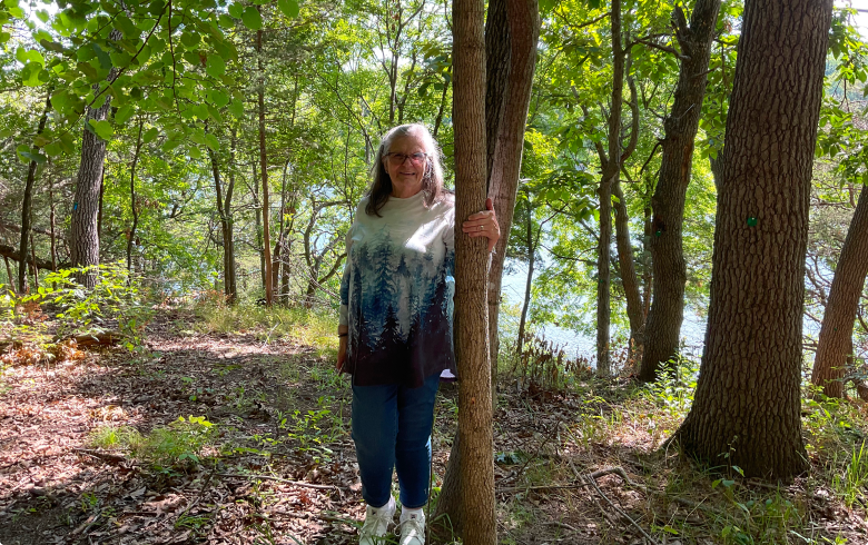 a woman stands by her husbands memorial tree in better place forests rock river memorial forest